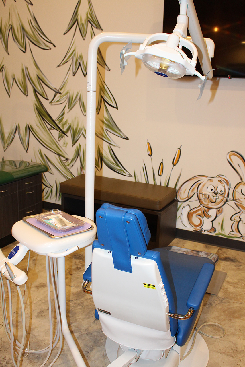 A dental chair with a blue drape on top, positioned in front of a dental practice setup with a chair and a desk.
