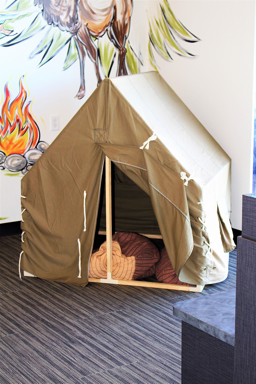 A small tent-like structure with a sleeping bag inside, placed indoors on a carpeted floor.